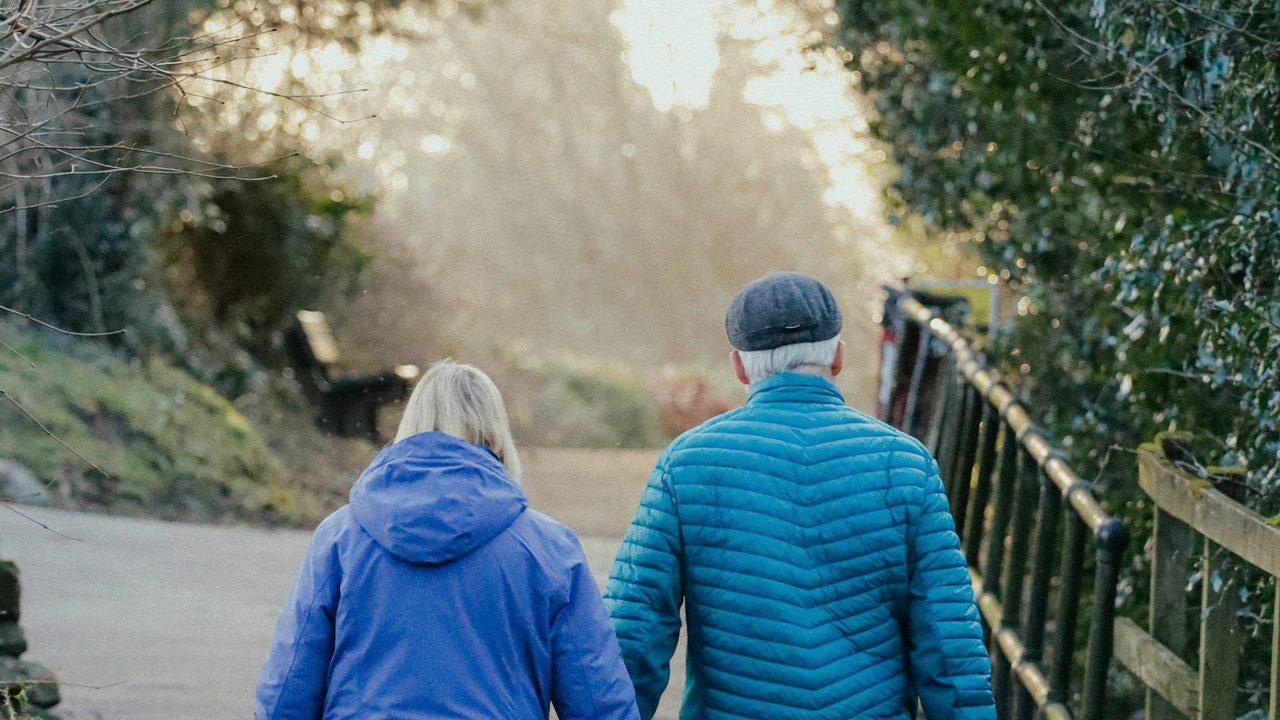 An older couple walking together at golden hour, in blue jackets — Walk Past Sixty, the senior edition
