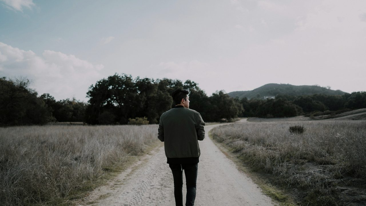 An adult walking through a park in morning light, head down in thought.